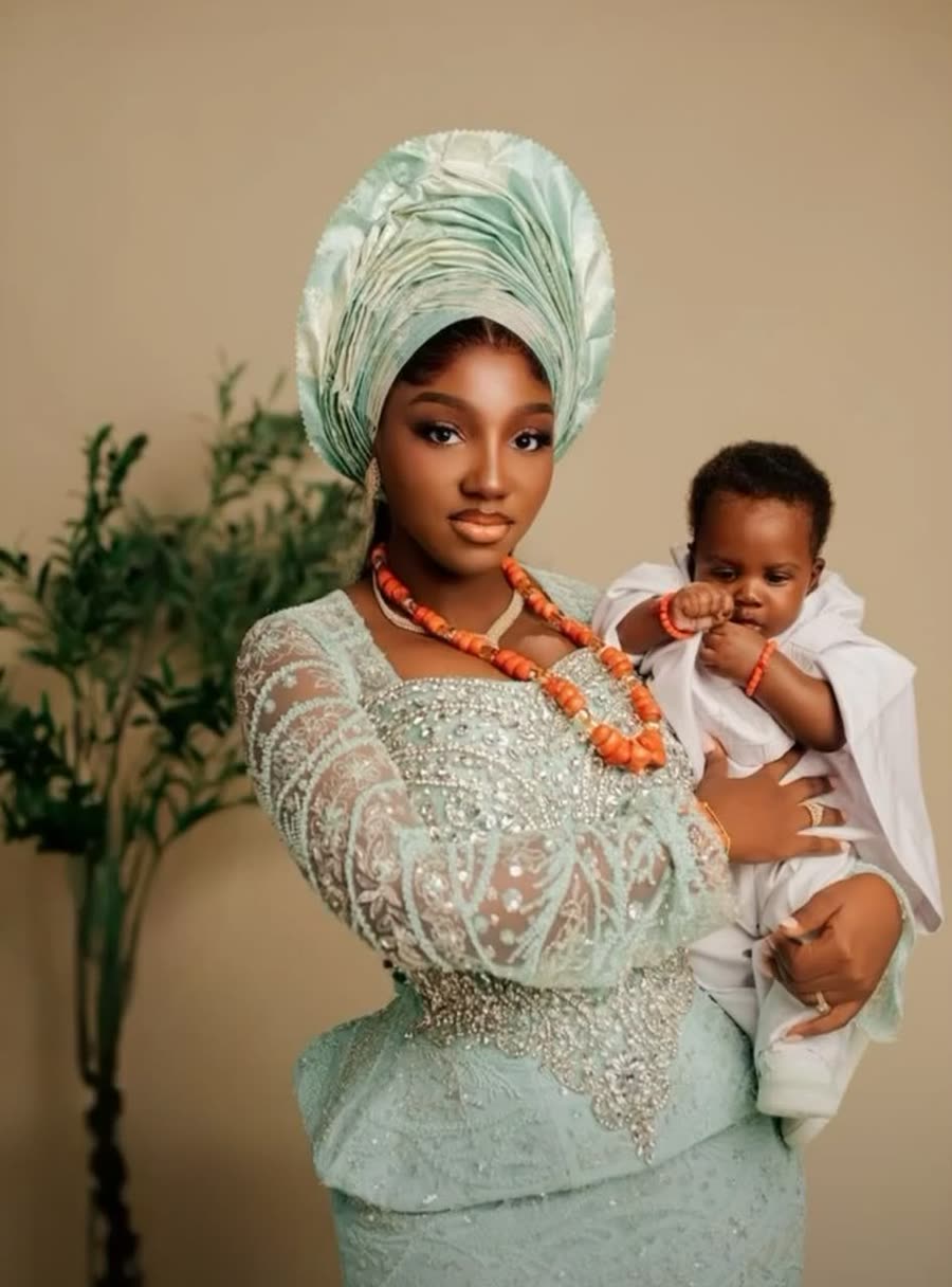 A mother in a traditional gele and lace outfit holding her baby
