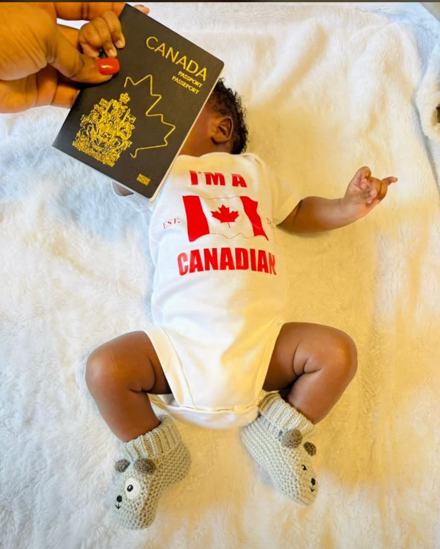 A baby in an 'I'm Canadian' onesie beside a Canadian passport