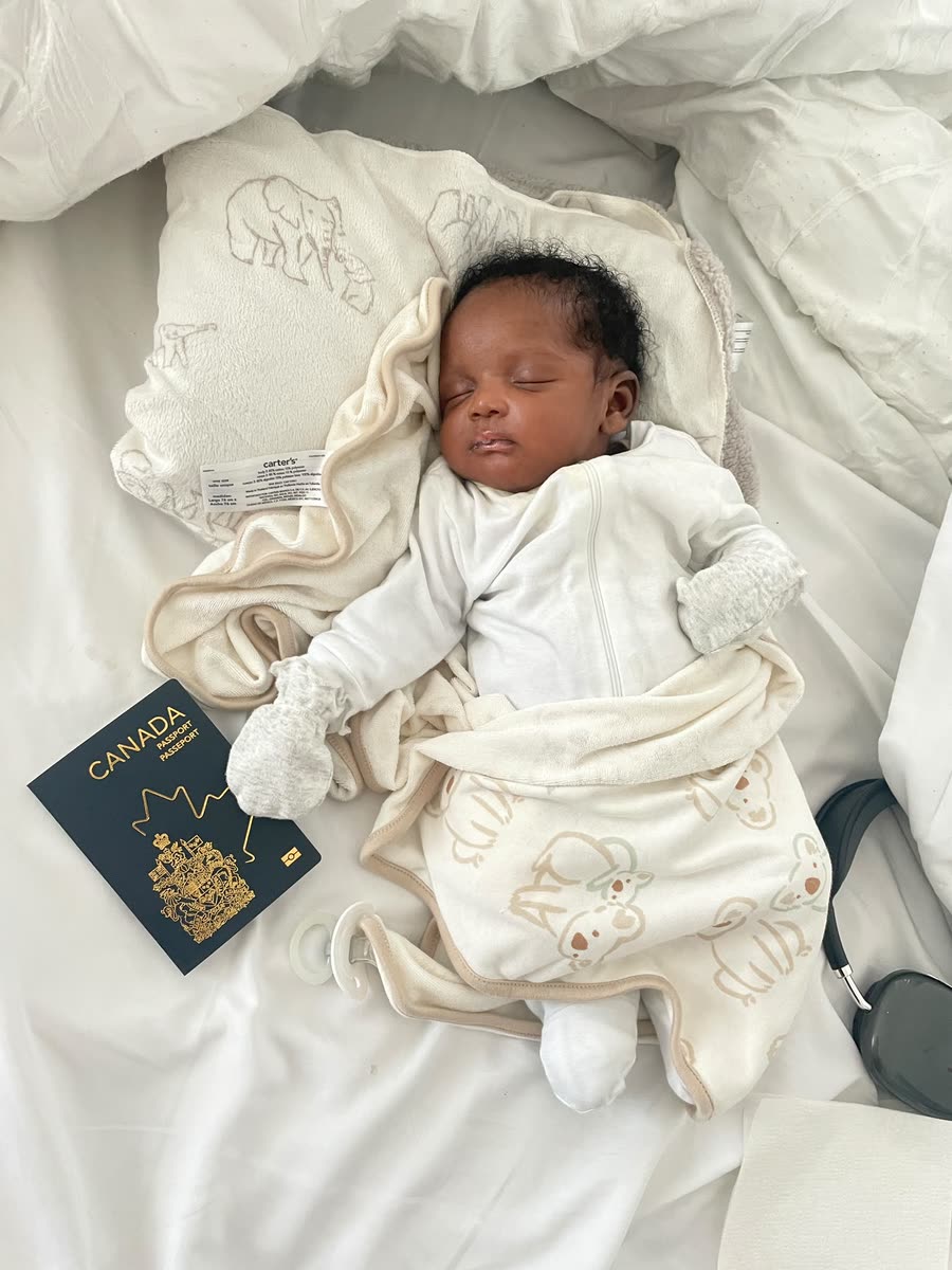 A sleeping newborn dressed in white beside a Canadian passport