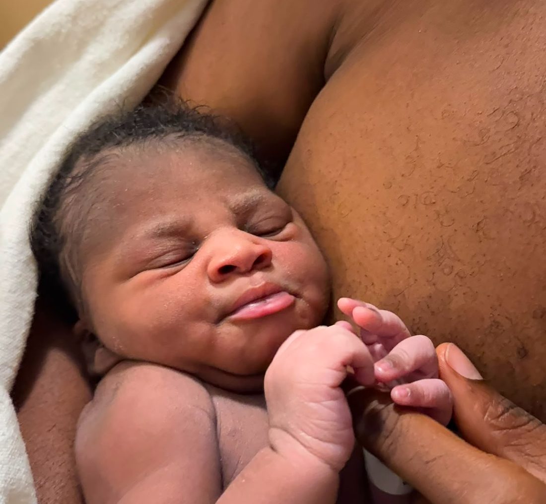 A newborn resting against a parent, holding their finger